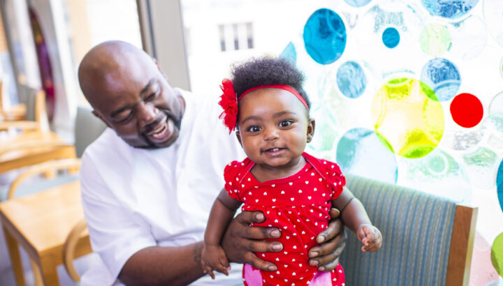 Man holding up toddler who is standing on a chair with whimsy circular background behind the chair.