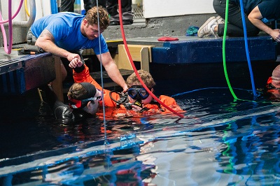 Patient ambassador Liam, wearing an orange wetsuit and scuba mask, enters the shark cage for his 12th dive at Point Defiance Zoo & Aquarium.