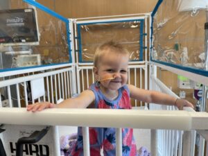 Baby in a hospital crib holding onto the rails and smiling for the camera