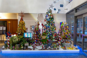 Four lit Christmas trees, decorated with dinosaurs, elves and toys, stand at the entrance of the MultiCare Tacoma General Hospital lobby. An LED arc showers presents and silver stars onto the trees and Santa below.