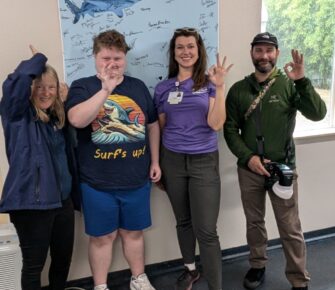 Patient ambassador Liam and his team of three other people make the diver’s OK hand signal and shark fin hand signal.