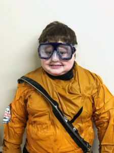 Liam, age 12 in October 2024, smiles in a soggy yellow wetsuit and eye goggles after a shark dive