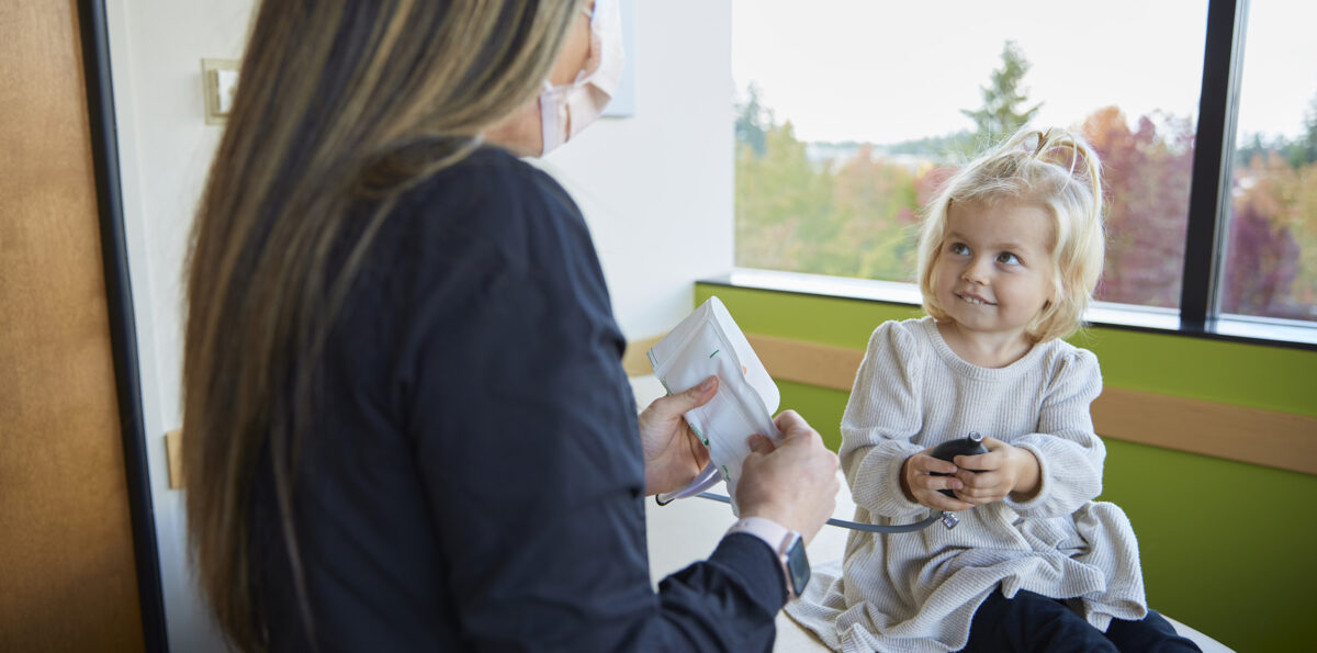 A young patient holds the bulb of a child-size blood pressure cuff during her doctor's office visit.