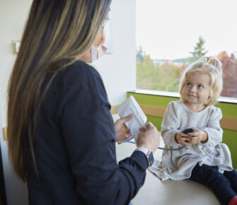 A young patient holds the bulb of a child-size blood pressure cuff during her doctor's office visit.