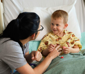 Boy smiles at nurse from hospital bed.