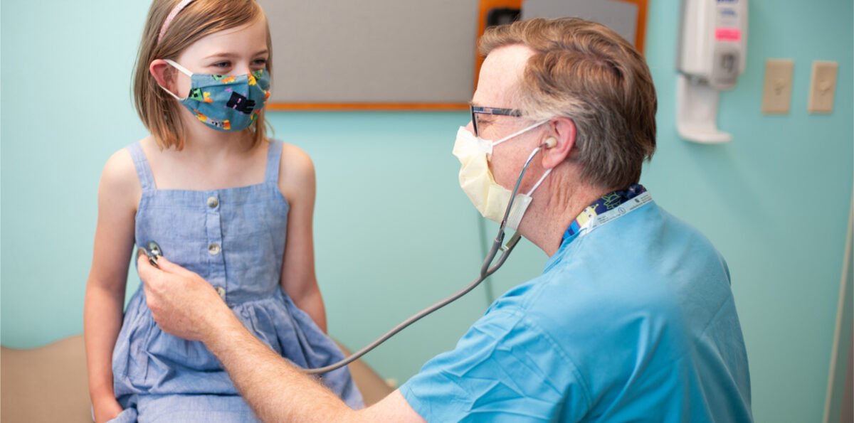 Girl wearing a mask having a check-up with a doctor.