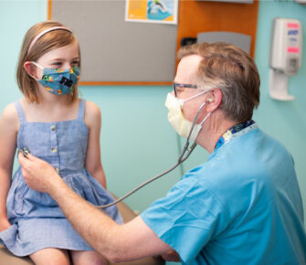 Girl wearing a mask having a check-up with a doctor.