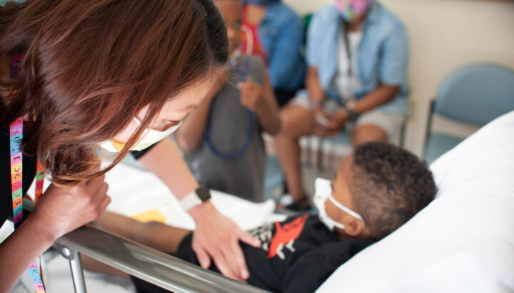 Masked, female doctor examining a young boy on a gurney.