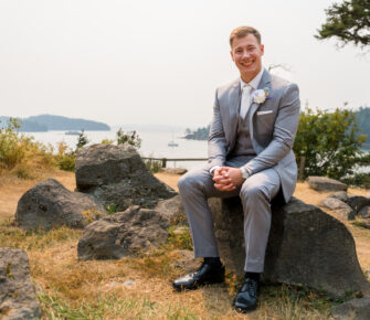 Young man wearing a gray suit sitting on a rock by the waterfront