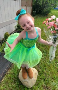 Baelah in a green ballet costume standing outside on a rock holding a bouquet of flowers