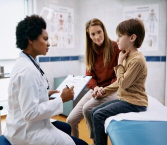 Doctor talks to child, who is touching his throat, and his mother