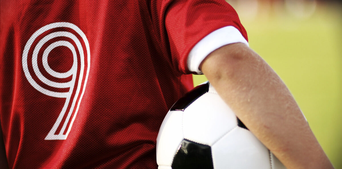 Youth soccer player in a red jersey with ball under their arm