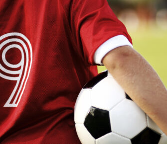 Youth soccer player in a red jersey with ball under their arm