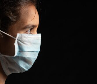 Young teenager girl with medical face mask in dark room at home quarantine due to covid 19 or coronavirus outbreak - concept of hope and fight to end virus crisis