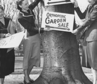 An old photo of women posting a garden sale sign.