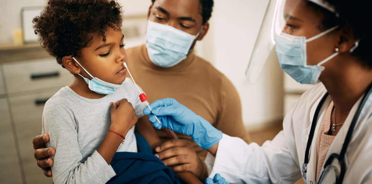 Doctor using cotton swab while PCR testing small boy at medical clinic.