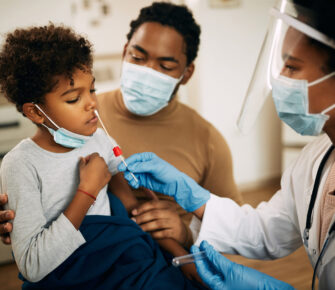 Doctor using cotton swab while PCR testing small boy at medical clinic.