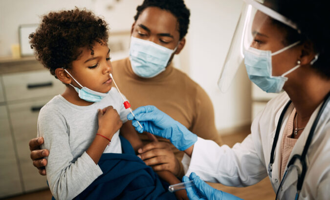 Doctor using cotton swab while PCR testing small boy at medical clinic.