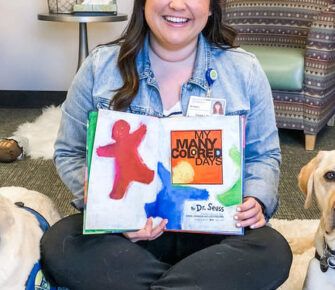 Woman holding book next to two dogs.