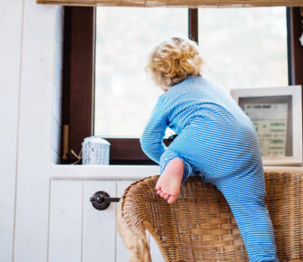 Toddler climbing a chair to get to a window.