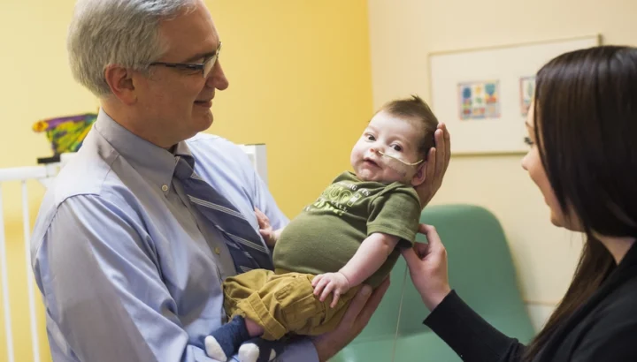 Dr. Raff holding an infant, with their mother in an exam room.