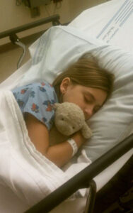 Emily hugging her stuffed animal and sleeping in the hospital