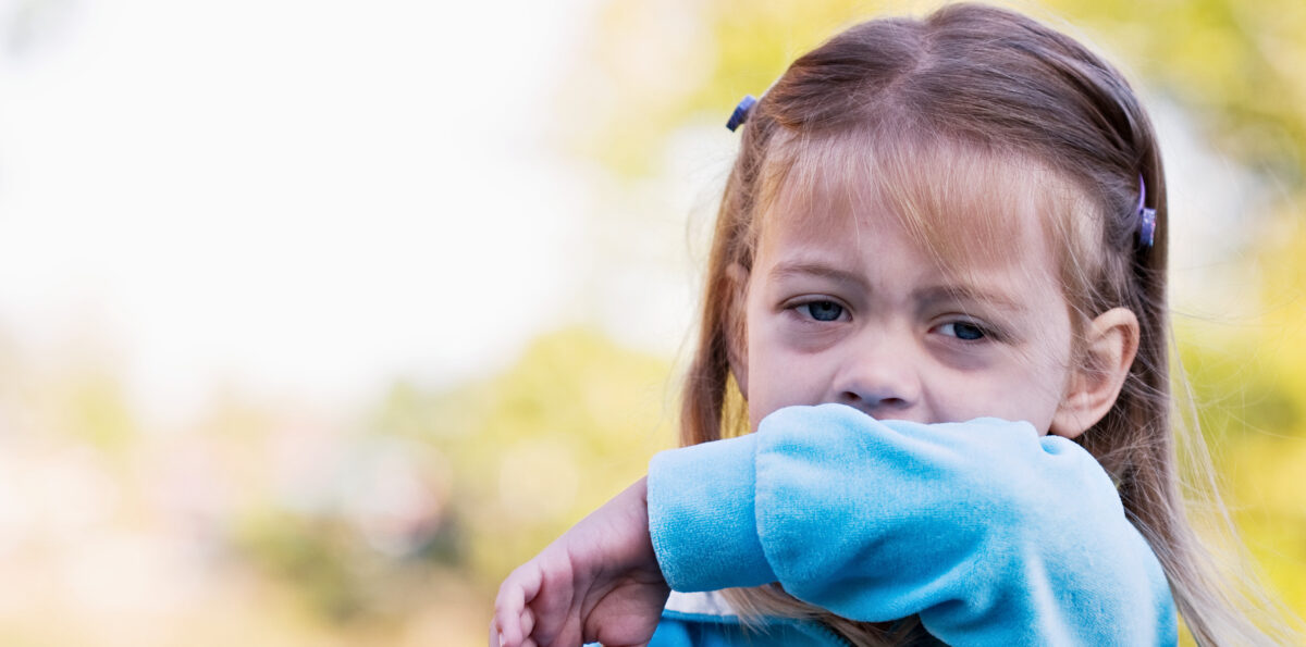 Little girl coughing or sneezing into her elbow.