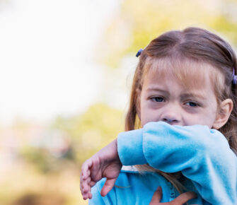 Little girl coughing or sneezing into her elbow.