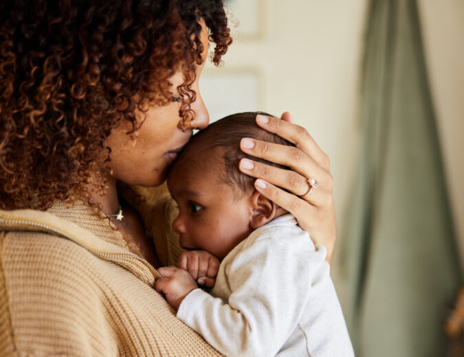 Close-up of a loving mother kissing her adorable little baby boy cradled in her arms at home