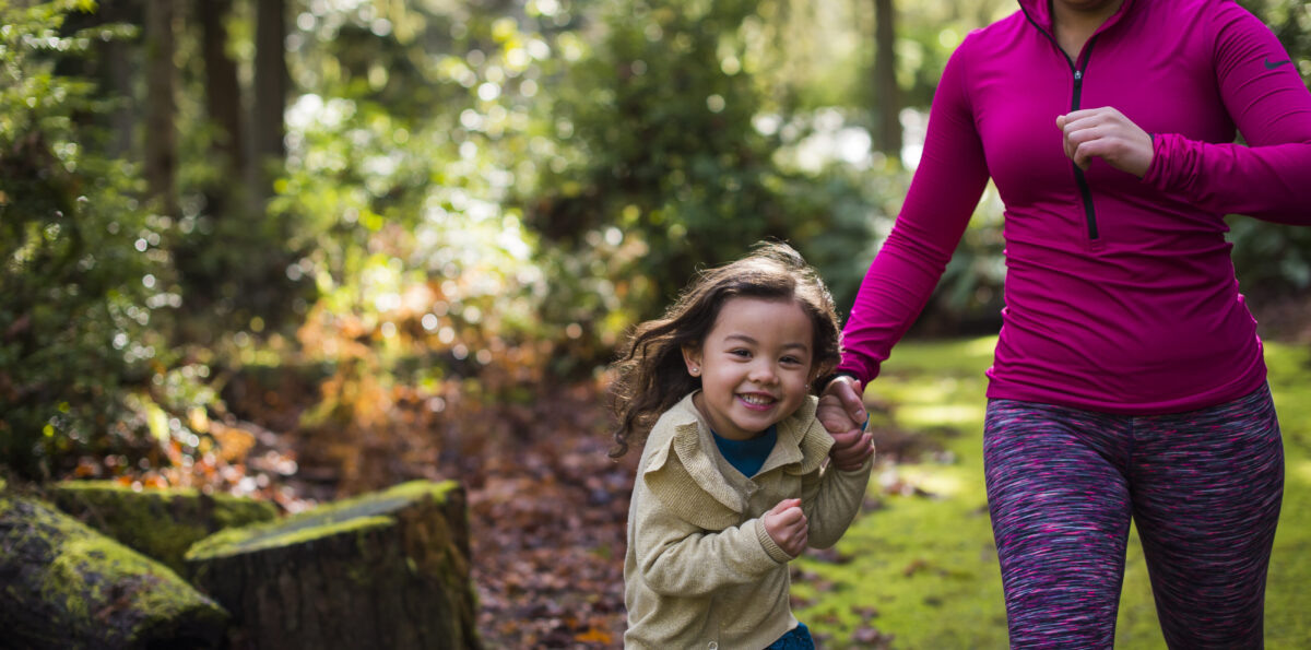 Mom and daughter run down a forested trail.