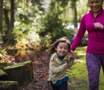 Mom and daughter run down a forested trail.