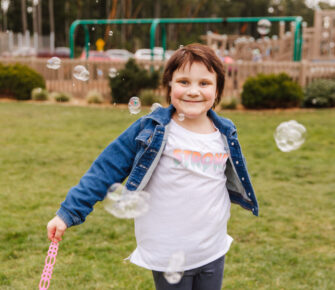 Lilith Kahn runs in a field with soap bubbles around her.