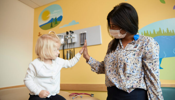 Young girl sitting in patient room on exam table, high-fiving her female doctor.