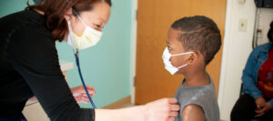 Young boy getting examined by doctor. Both wearing masks.