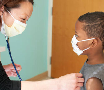 Young boy getting examined by doctor. Both wearing masks.