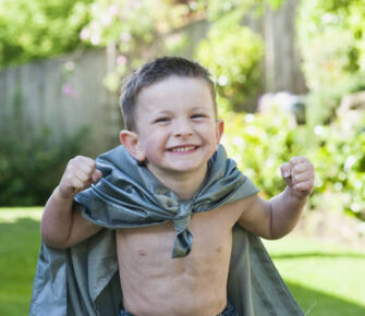 A little boy wearing a sheet as a cape.