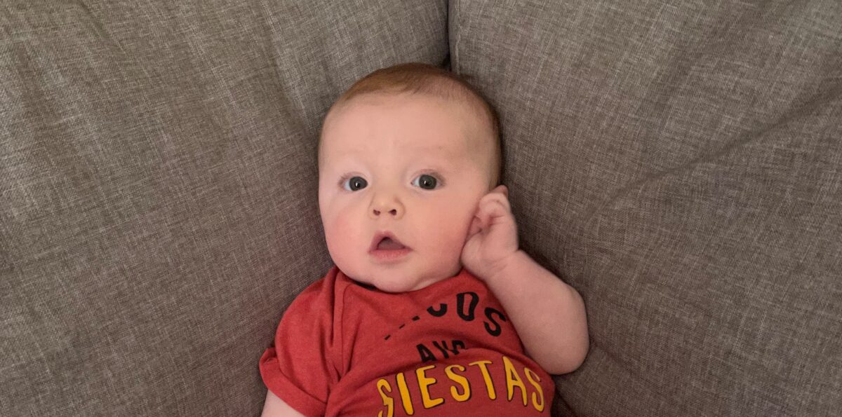 Baby Mercer sits propped into the corner of a couch.