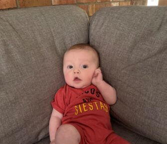 Baby Mercer sits propped into the corner of a couch.