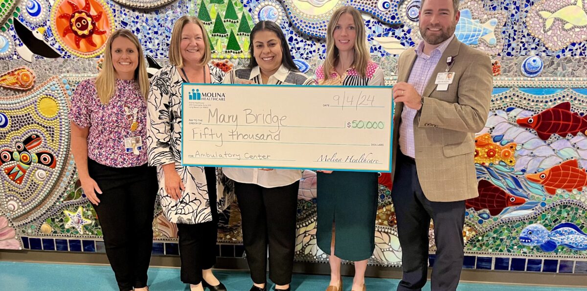 5 people hold a $50,000 check in front of the mural on the medsurg floor of Mary Bridge Children's Hospital.