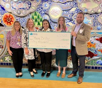 5 people hold a $50,000 check in front of the mural on the medsurg floor of Mary Bridge Children's Hospital.