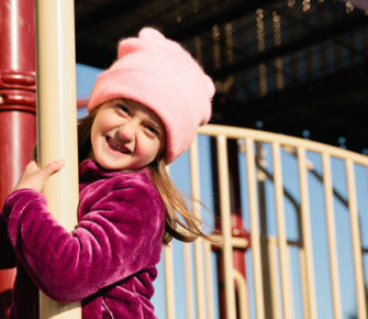 Girl in winter clothing playing on a playground.