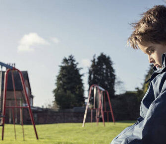 Sad child sitting on a bench near swings.