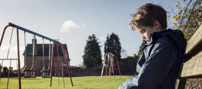 Sad child sitting on a bench near swings.