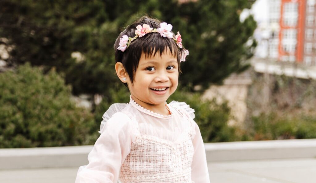 Little girl with flowers in her hair smiling.