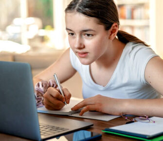 Kid reading notes on a computer and taking notes.