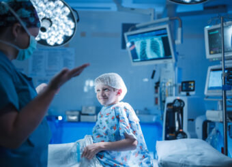 Boy smiles while talking to surgeon in operating room.