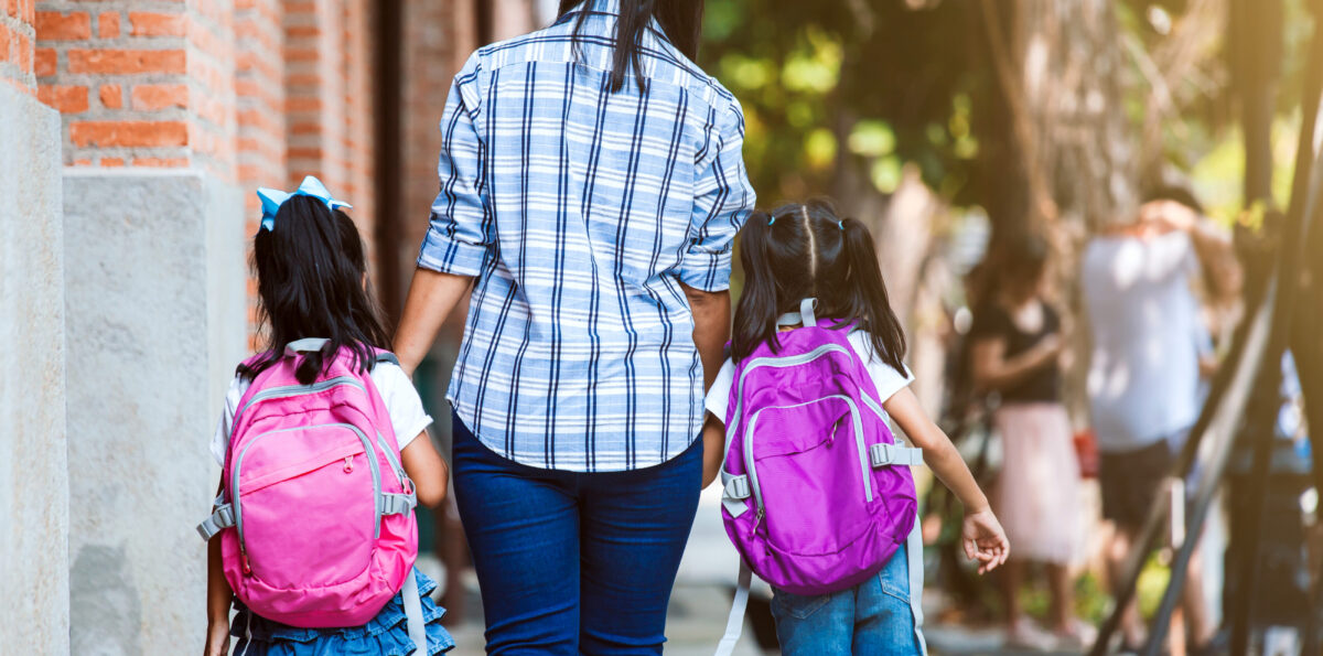 Mother and daughters with backpacks holding hand and going to school together.