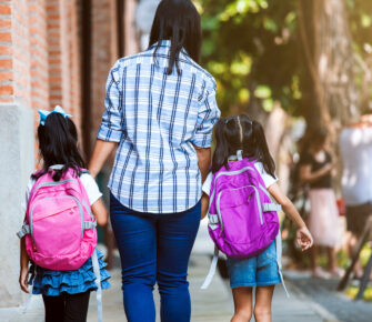 Mother and daughters with backpacks holding hand and going to school together.